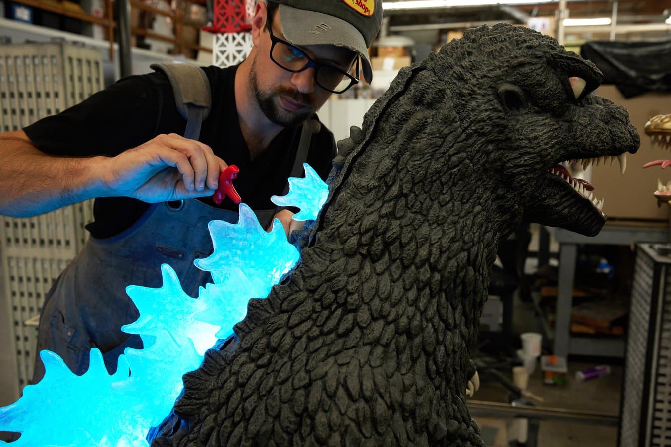 Person installing illuminated blue scales on the back of Godzilla